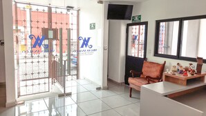 A reception area with a tiled floor, a reception desk, a chair, and a window with a view of the street. - Villas Analco Apartments (Puebla)