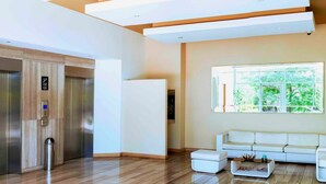 A modern lobby with a wooden floor, a white sofa, and a large window with a view of greenery. - Apartamento Vacacional en Barranquilla (Barranquilla)