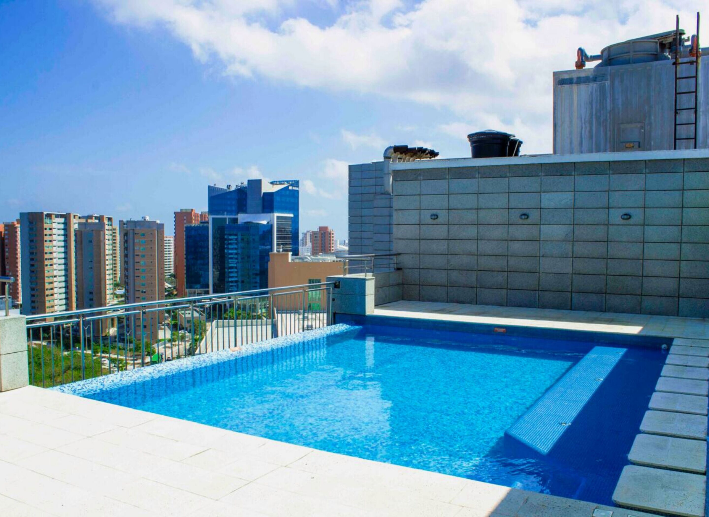 A rooftop swimming pool with a cityscape view, surrounded by high-rise buildings.