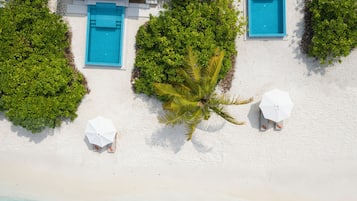 An aerial view of a resort with a pool, two beach umbrellas, and a palm tree.