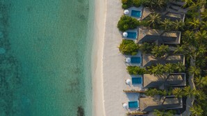 An aerial view of a beach resort with multiple bungalow-style accommodations, each with a thatched roof and surrounded by lush greenery. - Emerald Faarufushi Resort & Spa (Faarufushi)