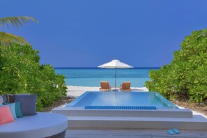 A poolside area with a view of the ocean, two lounge chairs, and an umbrella.