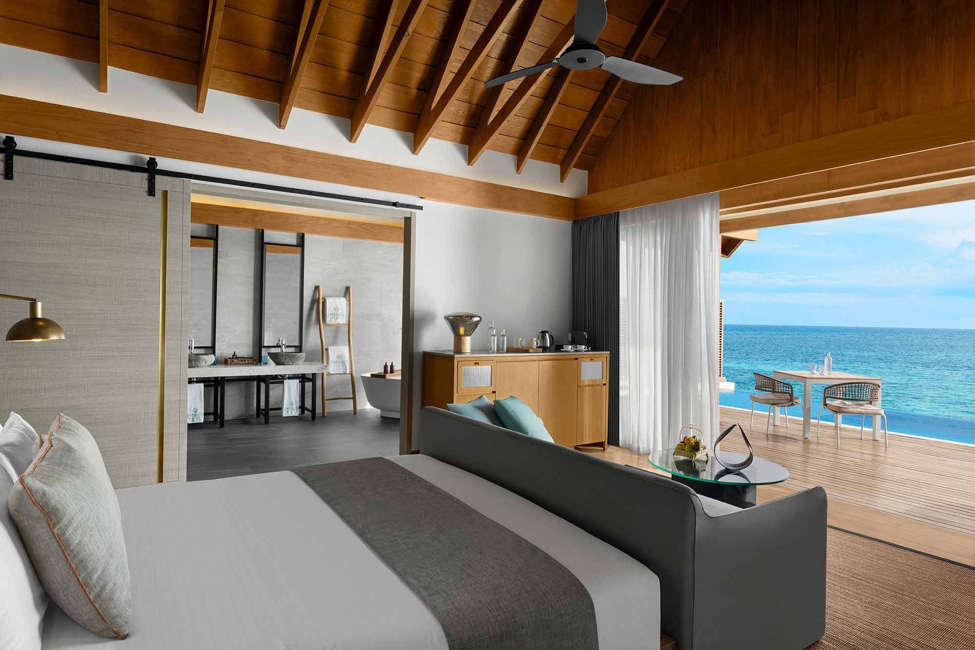 A hotel room with a bed, a sitting area, a kitchenette, and a view of the ocean.