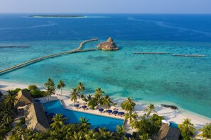 An aerial view of a resort with a swimming pool, palm trees, and a beach.
