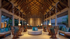 A spacious lobby with a high ceiling, wooden beams, and a central seating area with round tables and chairs. - Emerald Faarufushi Resort & Spa (Faarufushi)