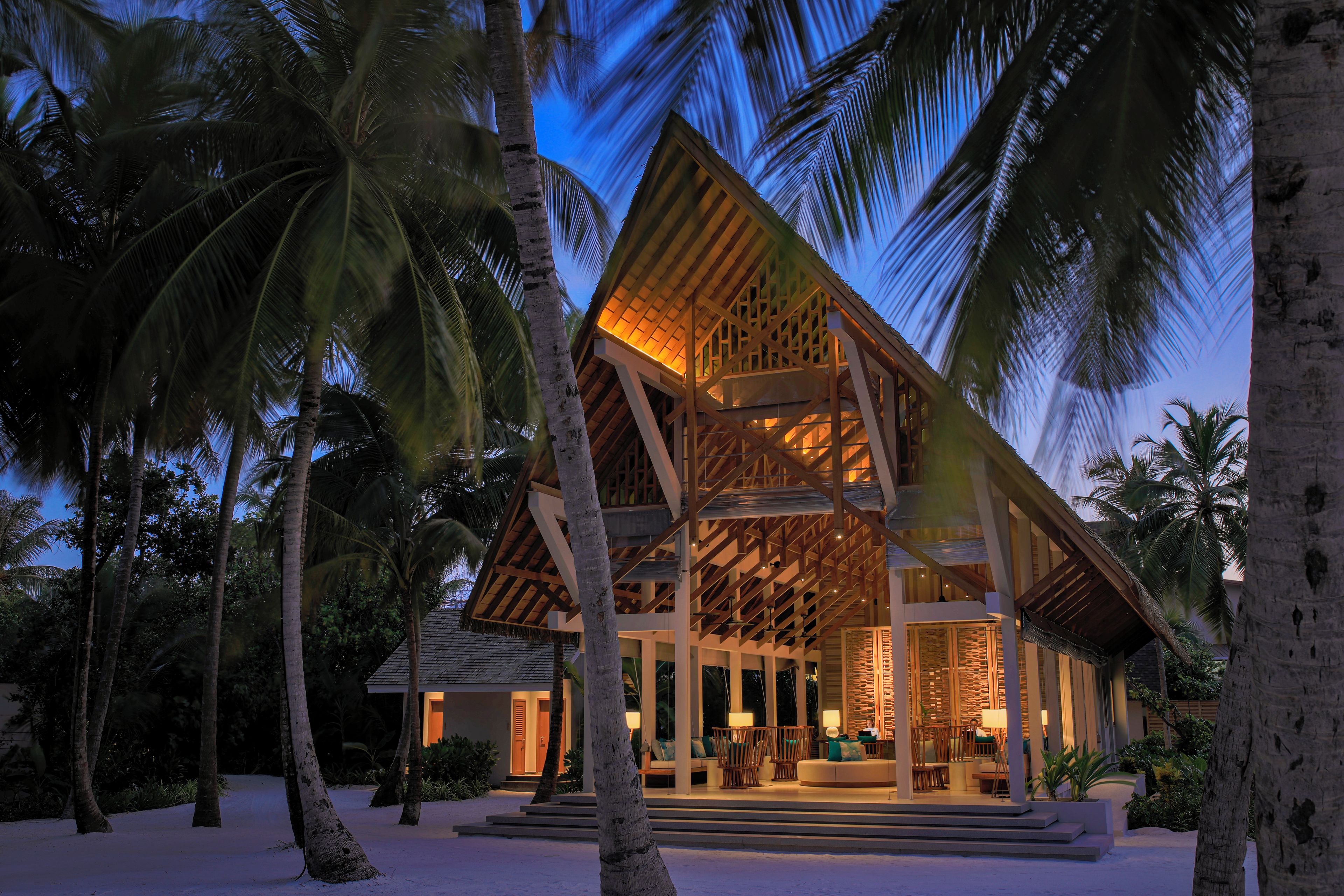 A beachfront resort with a wooden structure, palm trees, and a sandy beach.
