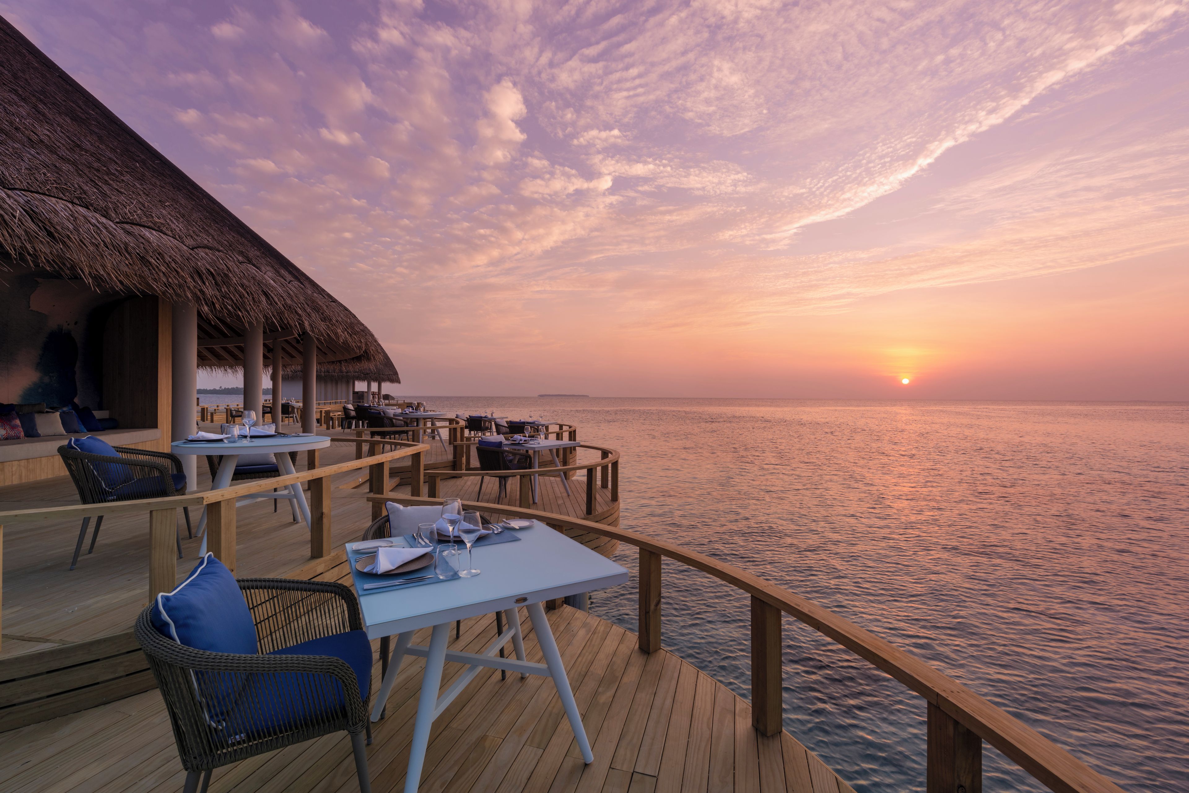 A deck with tables and chairs, overlooking the sea at sunset.