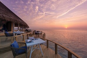 Una terraza con mesas y sillas, con vista al mar al atardecer.