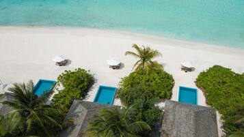 An aerial view of a beach with white sand, clear turquoise water, and several blue pool areas.