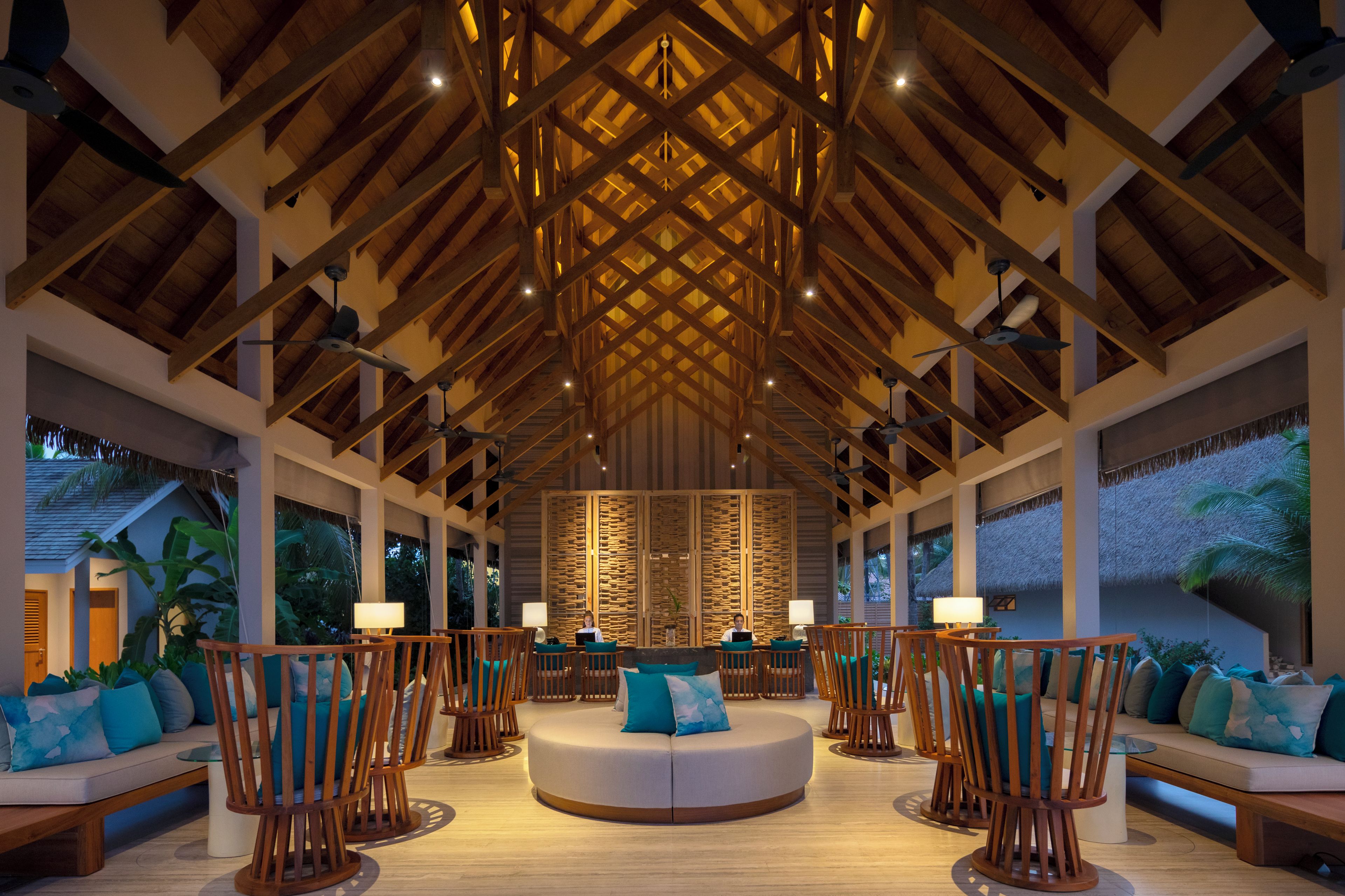 A spacious lobby with a high ceiling, wooden beams, and a central seating area with round tables and chairs.