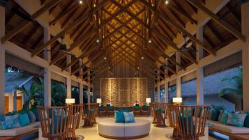 A spacious lobby with a high ceiling, wooden beams, and a central seating area with round tables and chairs.