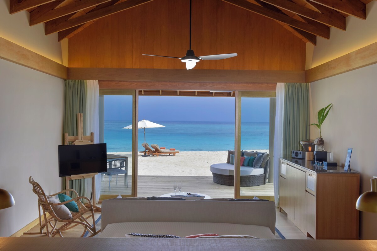 A bedroom with a large bed, a TV, and a view of the beach.