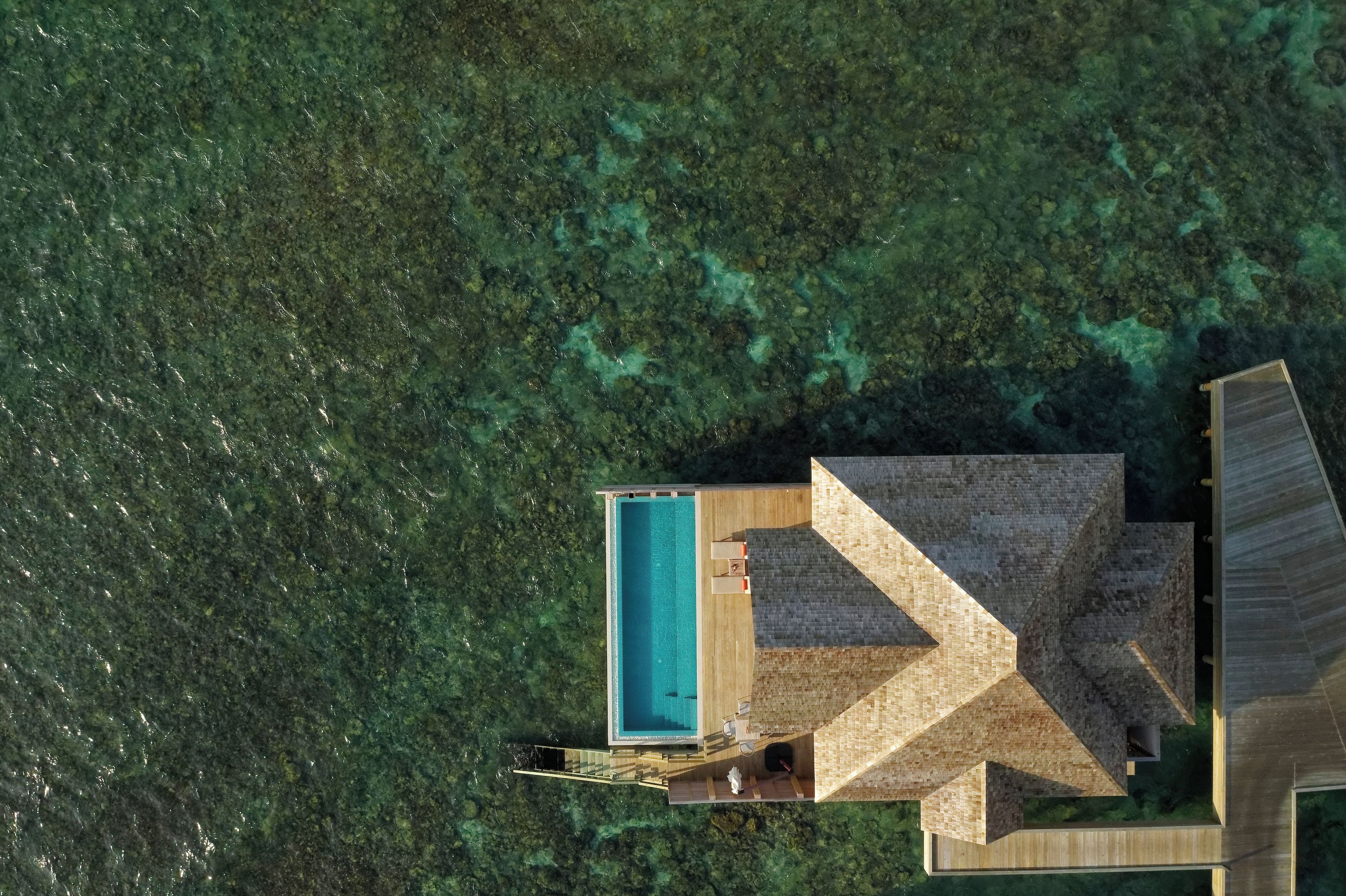 An aerial view of a resort with a swimming pool, wooden deck, and a small building structure.