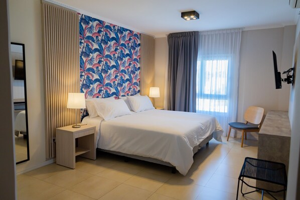 Una habitación de hotel con cama, mesitas de noche, una silla y un ventanal con cortinas.