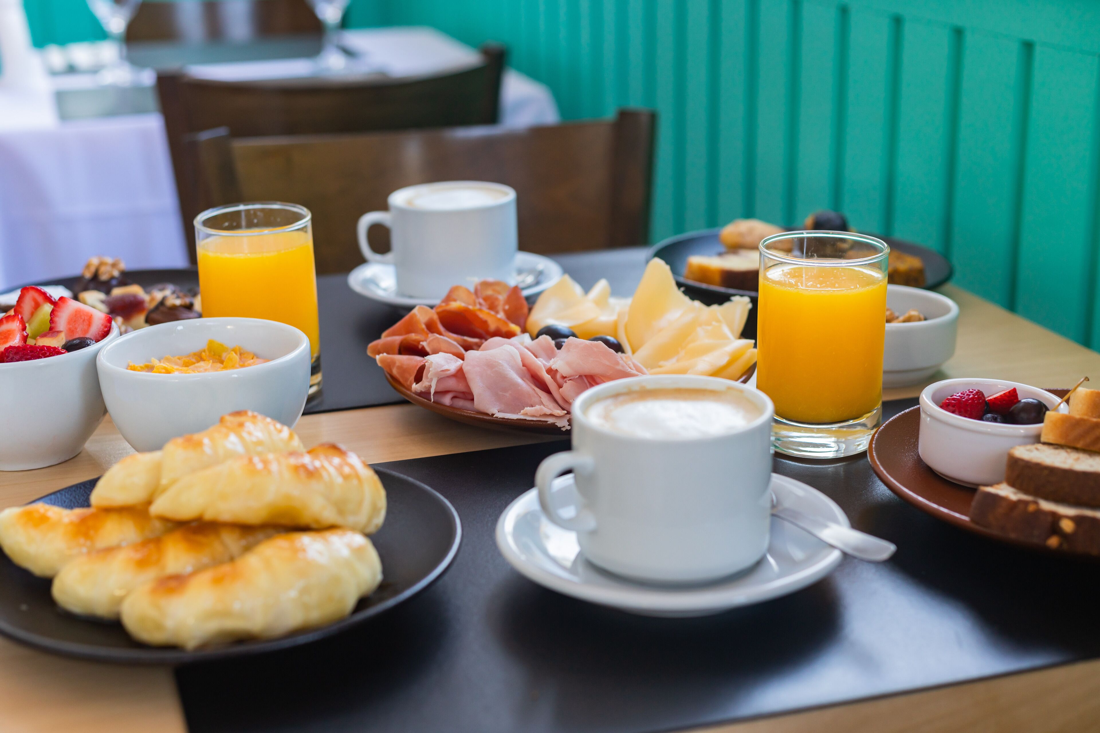 Desayuno con croissants, fruta, queso, jamón y café.
