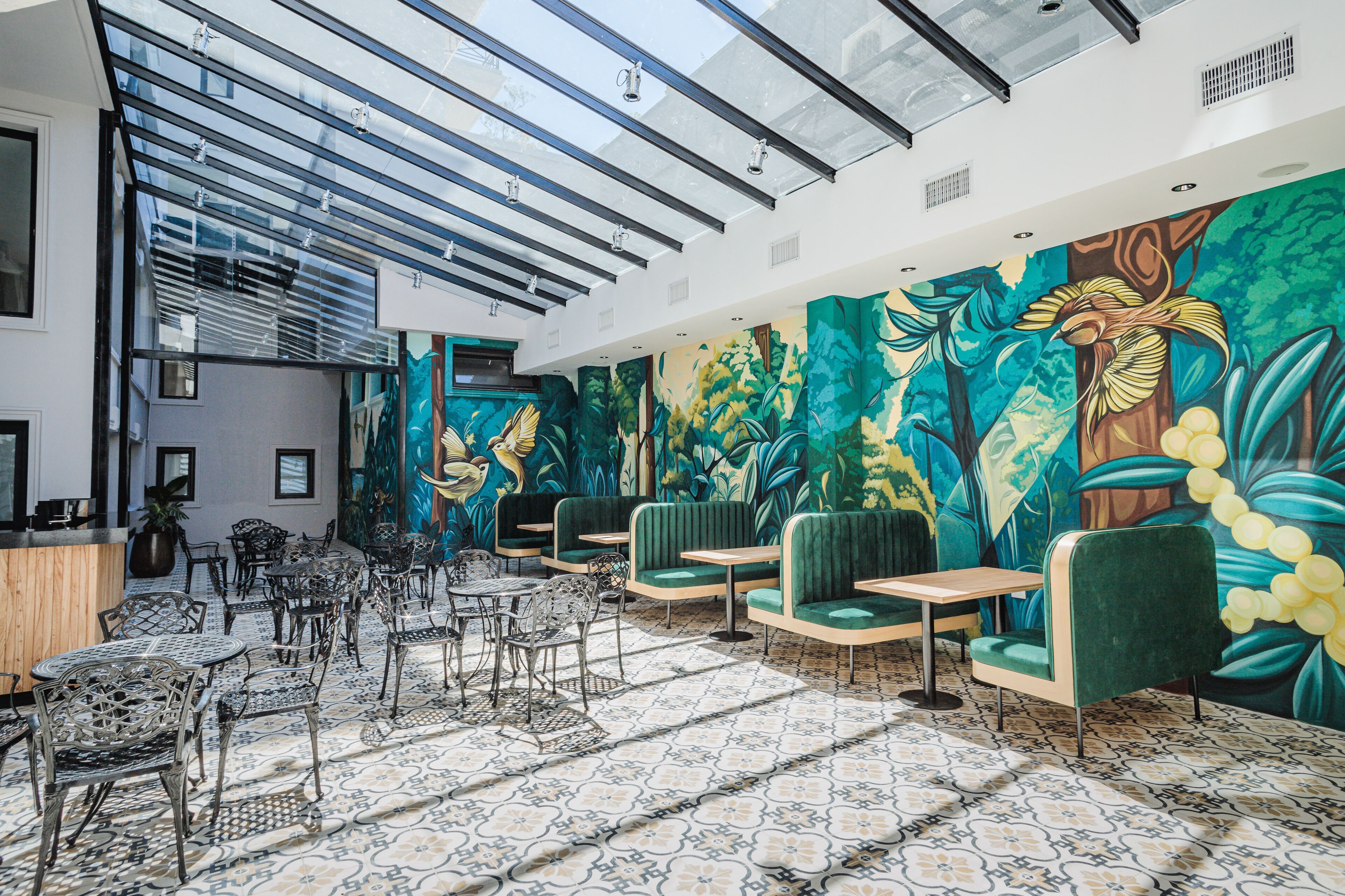 A spacious indoor area with a high ceiling, a large mural of tropical foliage, and a variety of seating arrangements including tables and chairs.