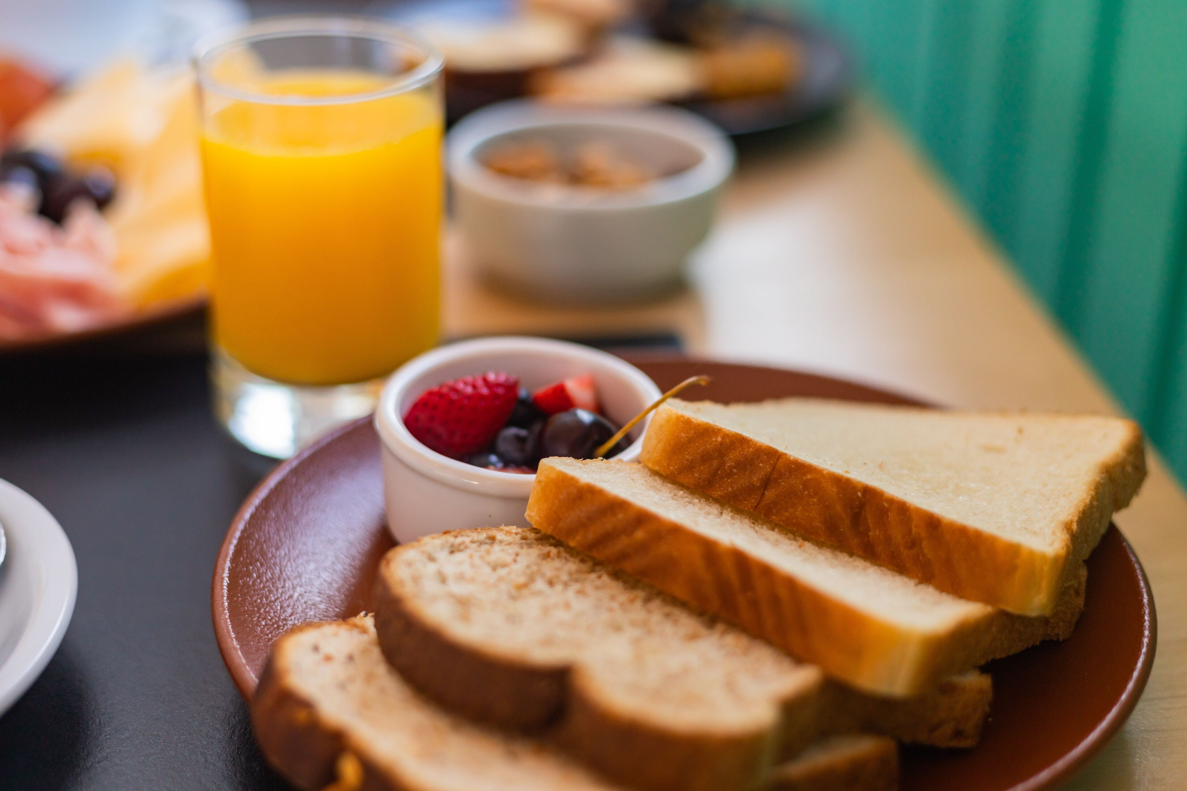 Ein Frühstücksbrett mit Toast, Orangensaft im Glas und einer Schale Beeren.