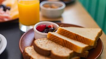 Una bandeja de desayuno con tostadas, un vaso de jugo de naranja y un bol de frutos rojos.