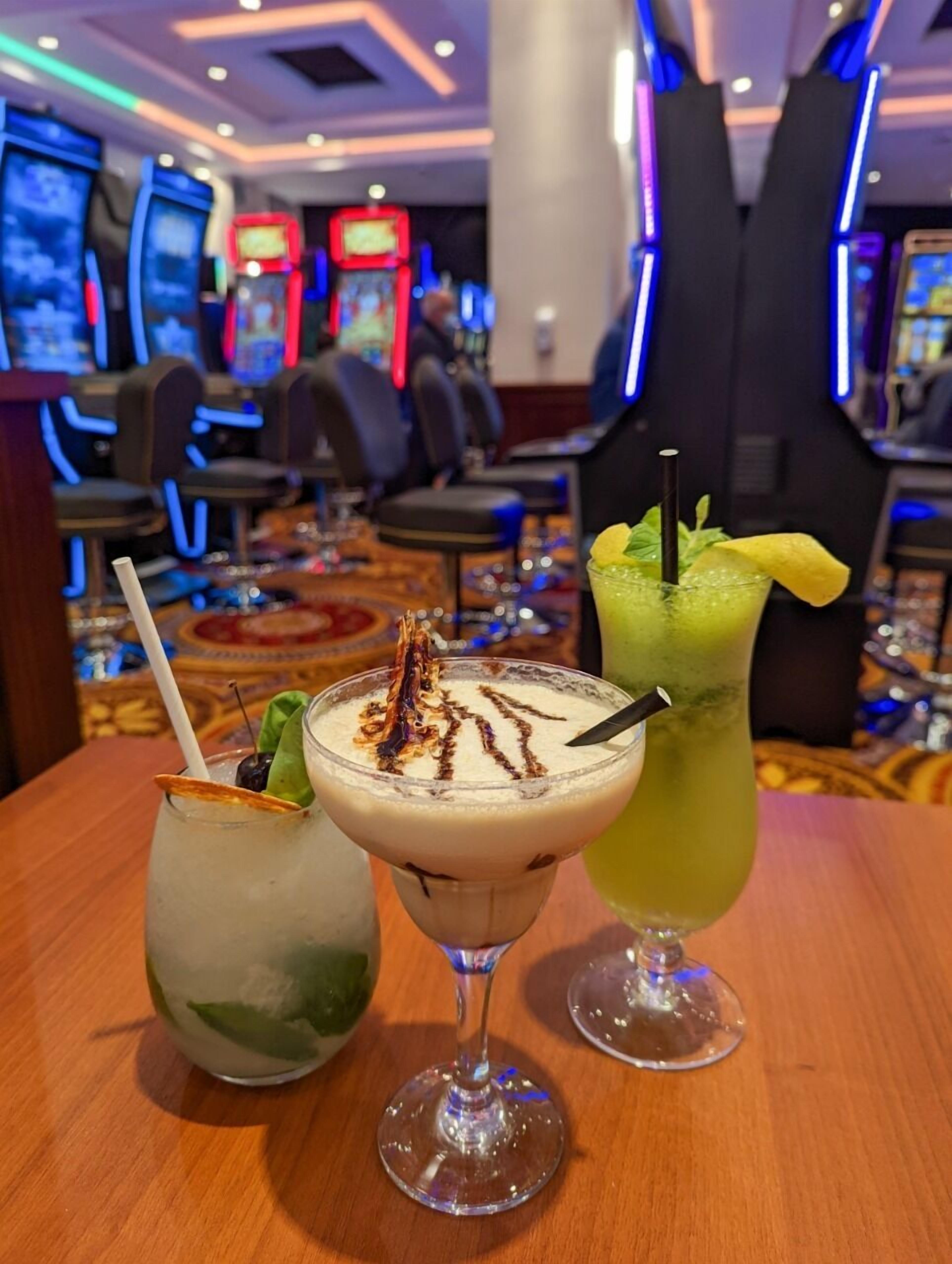 Three cocktails on a table in a bar area with arcade machines in the background.