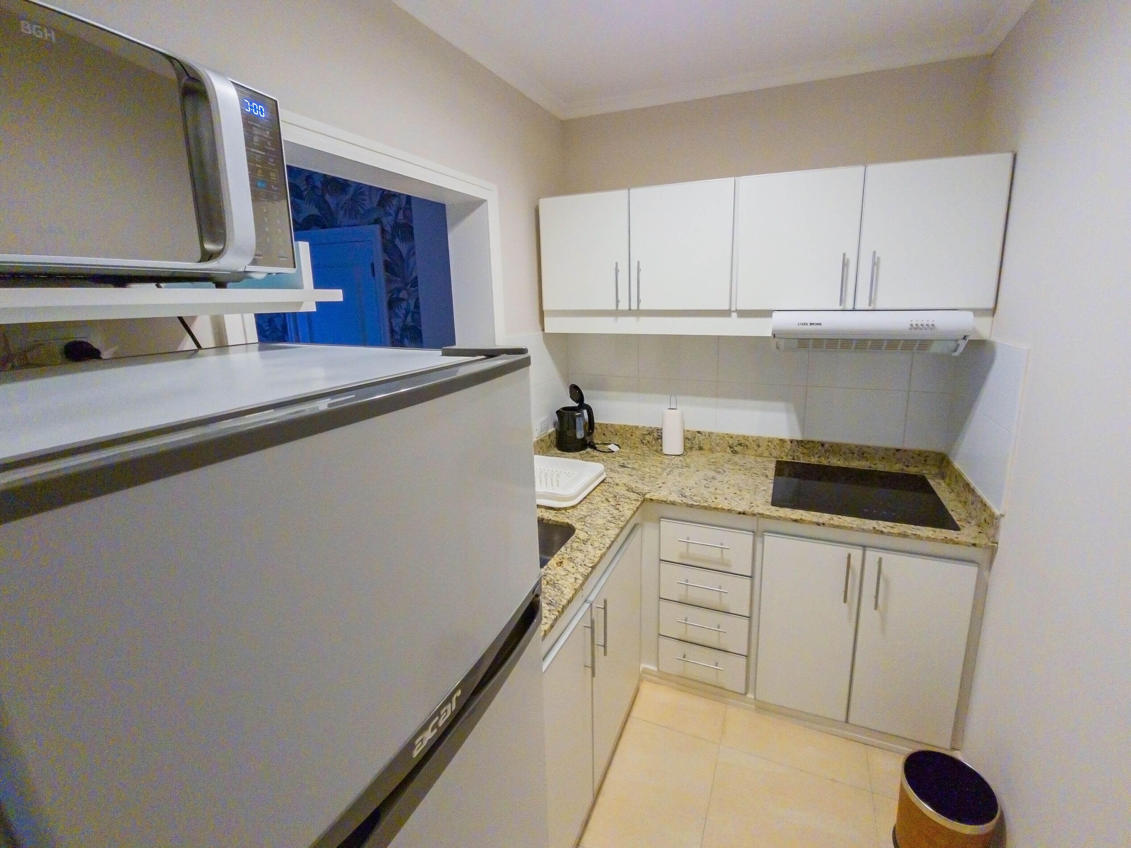 A compact kitchen with white cabinets, a microwave, a kettle, and a sink.