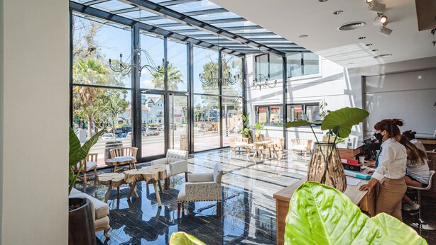 A modern interior with a glass ceiling, a seating area with tables and chairs, and a large green plant. - Garden Suites Pinamar (Pinamar)