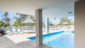 A pool area with lounge chairs and umbrellas, surrounded by a low wall and trees. - Garden Suites Pinamar (Pinamar)