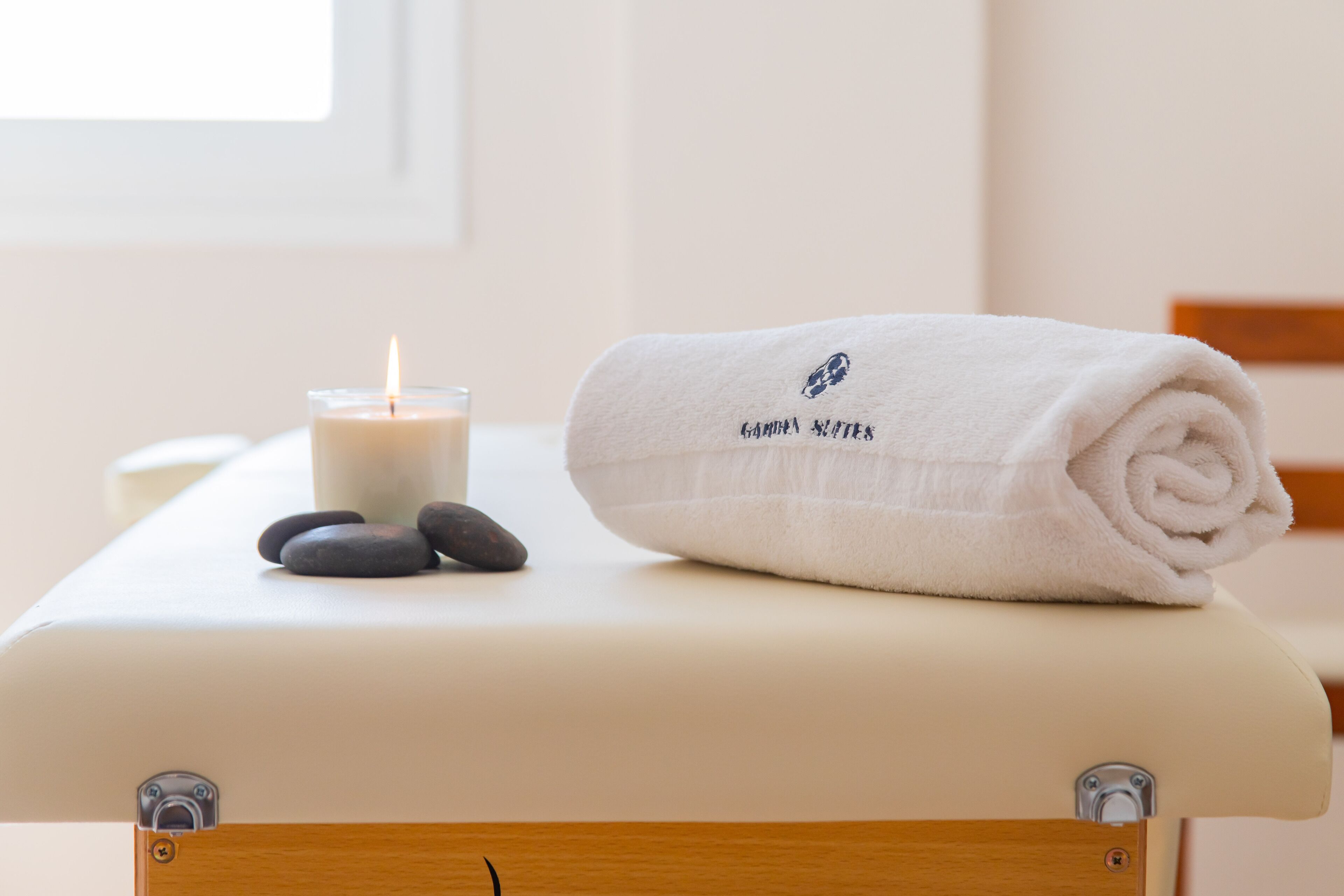 Une table de massage avec une serviette roulée et une bougie allumée.