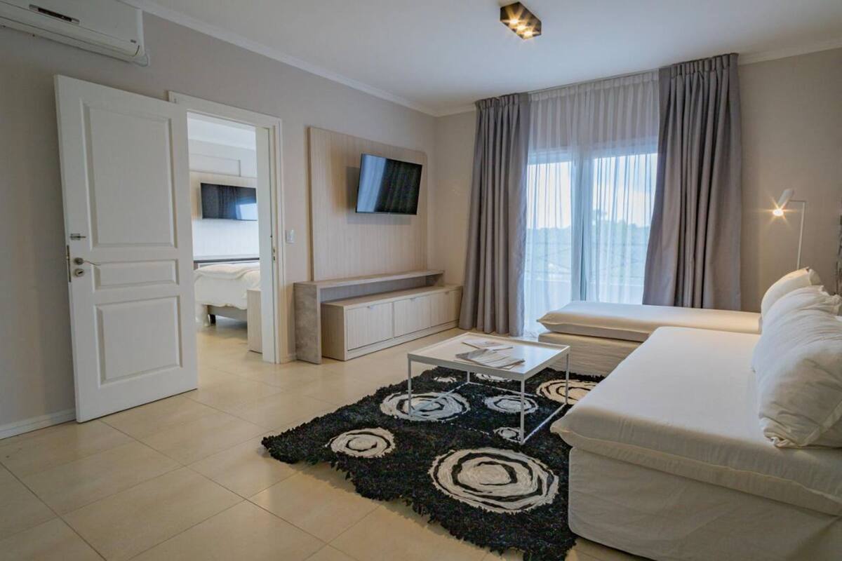 Ett modernt hotellrum med en säng, en soffa, en tv som är monterad på väggen och ett stort fönster med gardiner.