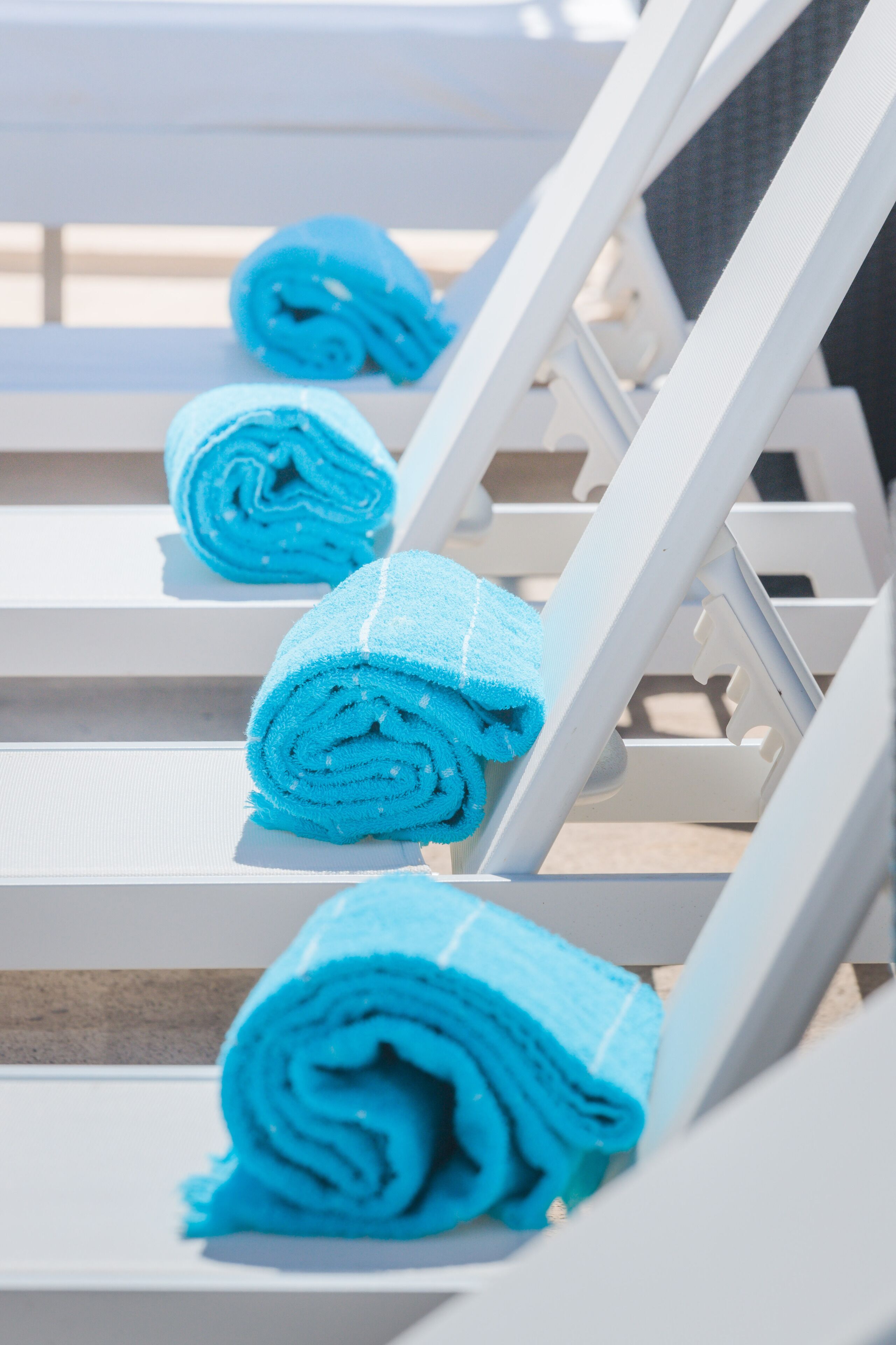 A row of white lounge chairs with blue towels neatly rolled and placed on them.