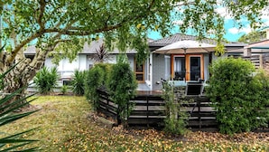 A house with a covered patio, a wooden fence, and a well-maintained garden with various plants and trees. - Nautilus on the Inlet (Inverloch)