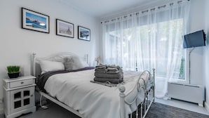 A neatly arranged bedroom with a bed, bedside table, and a window with sheer curtains. - Nautilus on the Inlet (Inverloch)