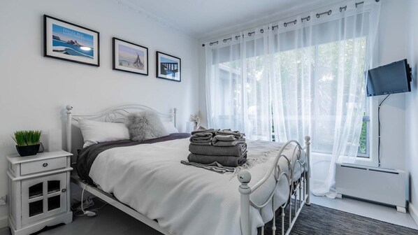 A neatly arranged bedroom with a bed, bedside table, and a window with sheer curtains. - Nautilus on the Inlet (Inverloch)