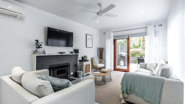A modern living room with a fireplace, a flat-screen TV, and a ceiling fan. - Nautilus on the Inlet (Inverloch)