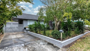 A residential property with a grey house, a fenced driveway, and a well-maintained garden with various plants and a mailbox. - Nautilus on the Inlet (Inverloch)