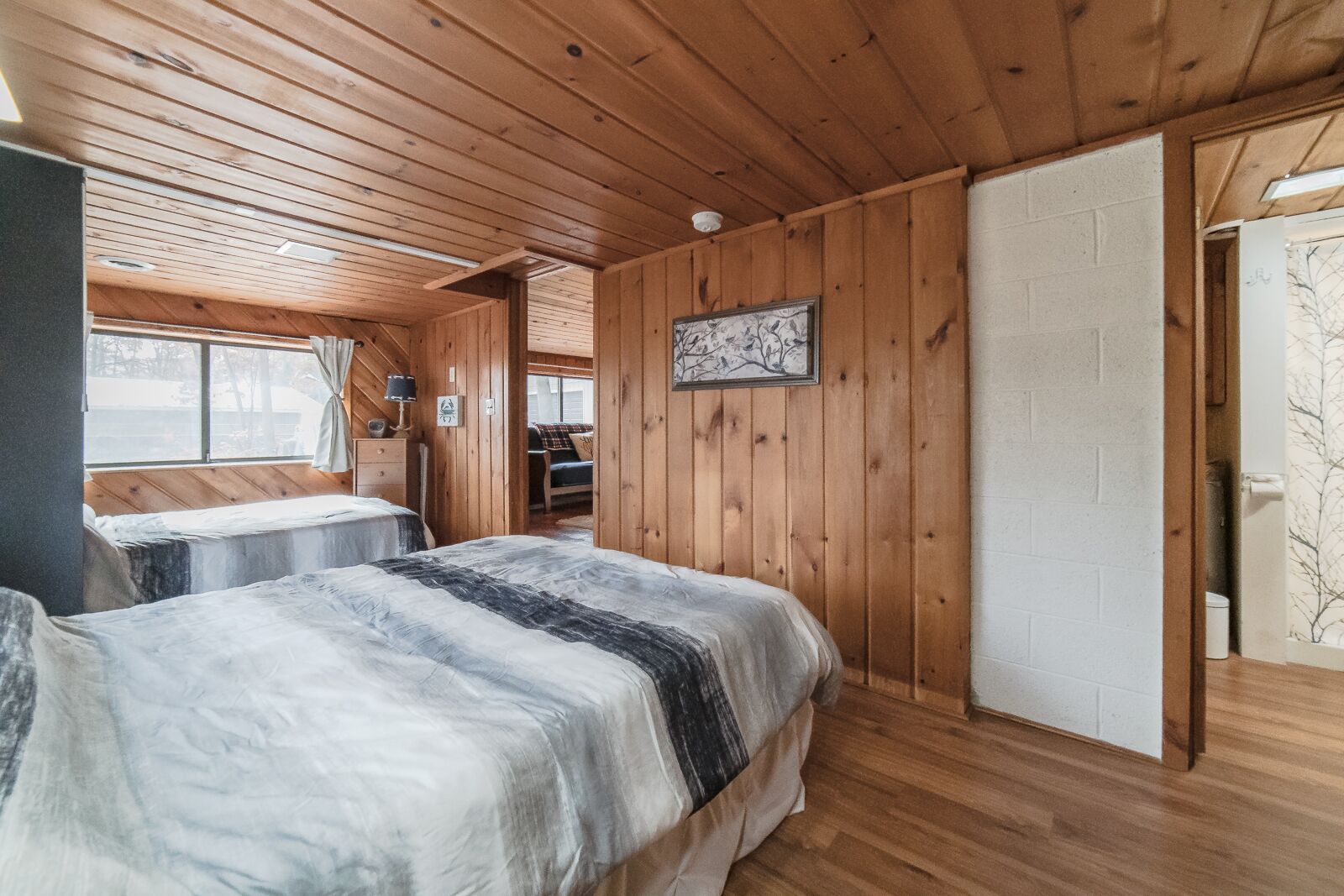 Eine Holzhütte mit zwei Betten, Holzwänden, einer weißen Tür und einem Fenster.