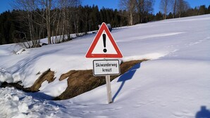 A warning sign in a snowy landscape with a clear blue sky.
