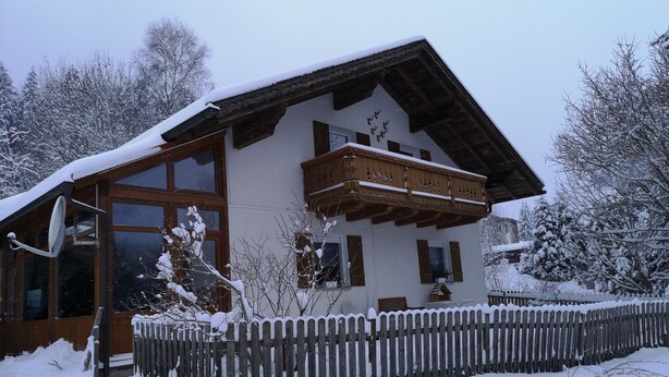 A chalet-style building with a wooden balcony, large windows, and a snow-covered roof.