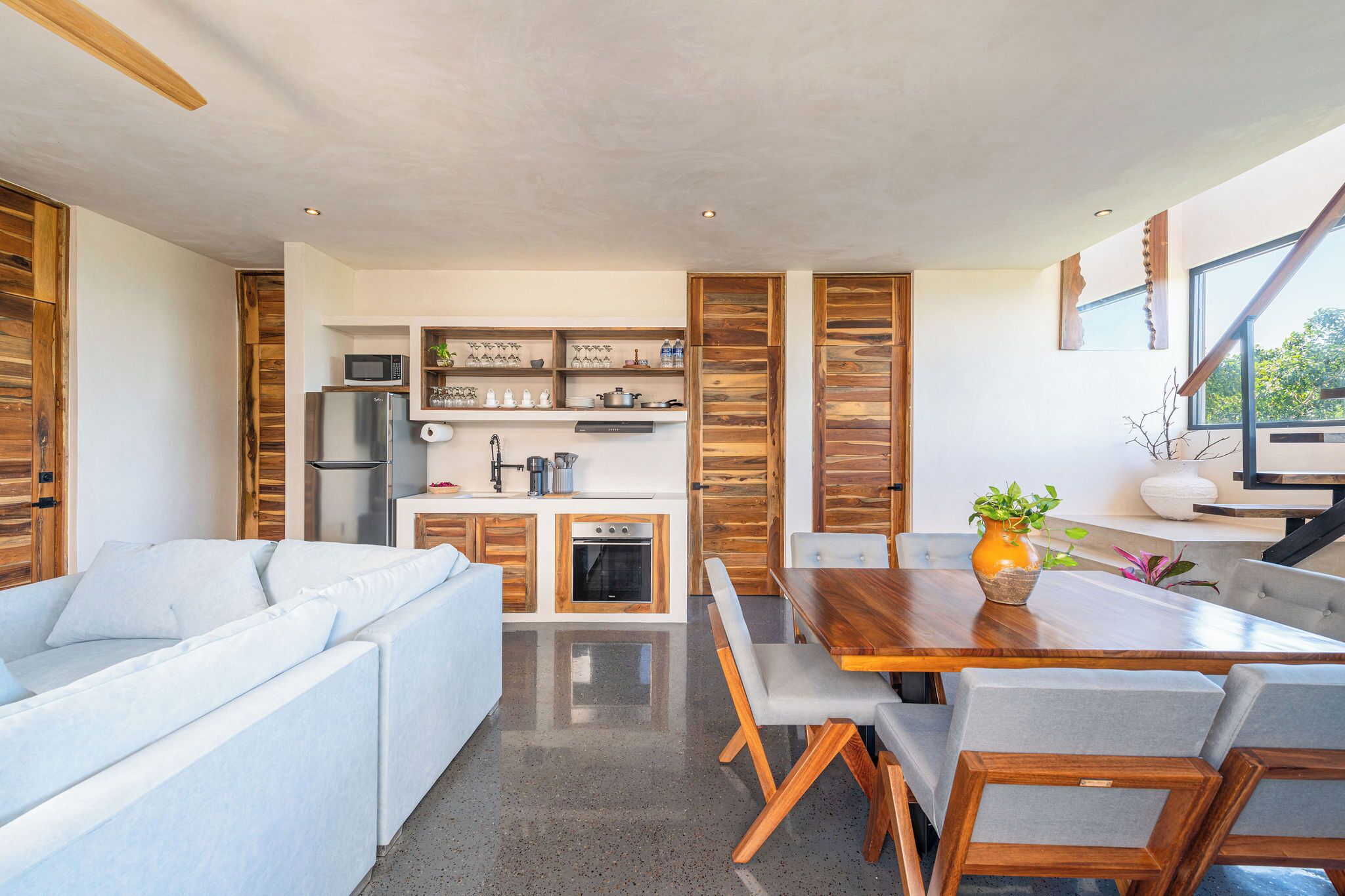 Et moderne køkken med indbyggede hårde hvidevarer, et spiseområde med et træbord og stole, og en sofa i opholdsstuen.