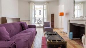 Un soggiorno con un divano viola, un tavolino, un camino e un balcone con ringhiera.