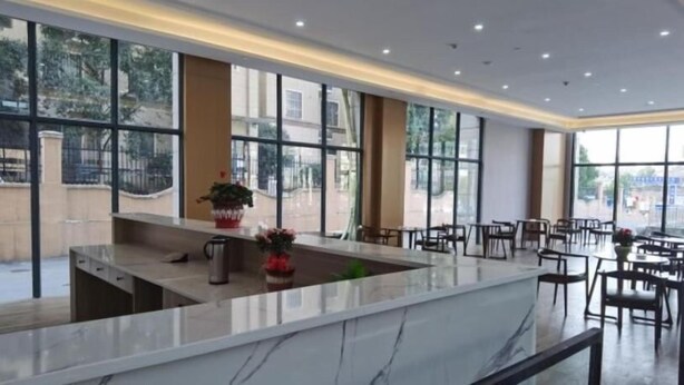 Un moderno vestíbulo de hotel con una recepción de mármol, ventanas amplias y un área de estar con mesas y sillas.