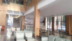 Un vestíbulo amplio con techo alto, una zona de estar con sillones y un sofá, y grandes ventanales que ofrecen vistas al exterior.