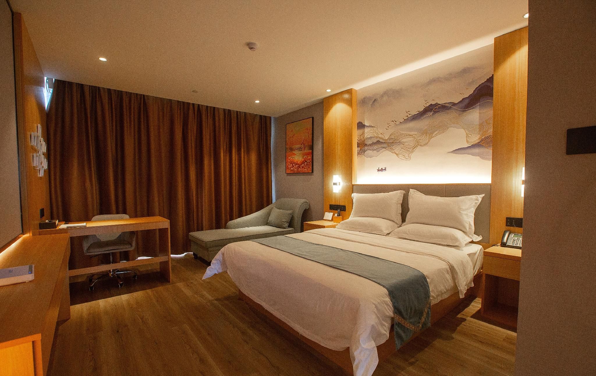 A hotel room with a large bed, a desk, a chair, and a wall with a painting.