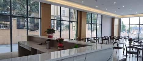 A modern hotel lobby with a marble reception desk, seating area, and large windows offering views of the outside.