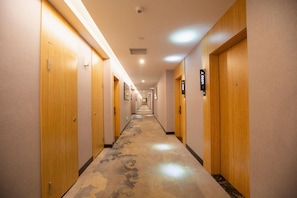 Un pasillo de hotel con puertas de madera, placas de identificación de habitaciones numeradas y piso alfombrado.