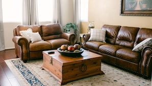 Ein Wohnzimmer mit zwei braunen Ledersofas, einem Holztisch mit Früchten und einem gemusterten Teppich.