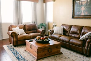 A living room with two brown leather sofas, a wooden coffee table with fruit, and a patterned rug.