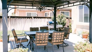 Eine Terrasse im Freien mit überdachter Essgegend, einem Grill und einem Holzzaun im Hintergrund.