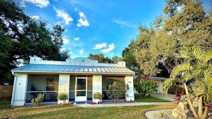 A single-story house with a flat roof, a front porch, and a small garden area with various plants and a palm tree. - Bungalow w/ Heated Pool by Downtown & Beaches (Sarasota)