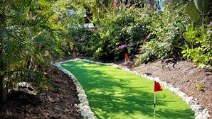 A miniature golf course with a green putting surface, red flags marking the holes, and a surrounding border of white stones. - Bungalow w/ Heated Pool by Downtown & Beaches (Sarasota)