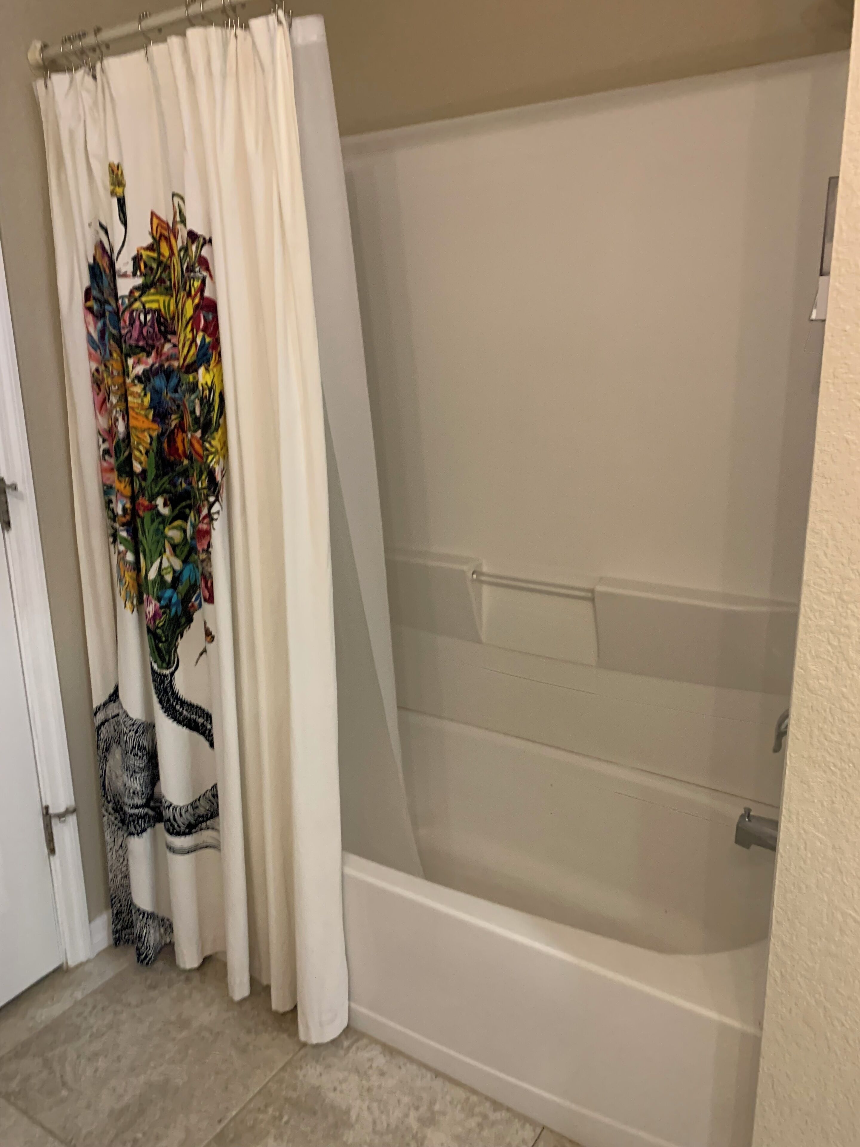 Une salle de bain avec une baignoire, un rideau de douche à motifs floraux et un carrelage au sol.